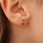 Orange-Ohrstecker am Ohr, runder Stein orange mit Blatt, filigranes Design.