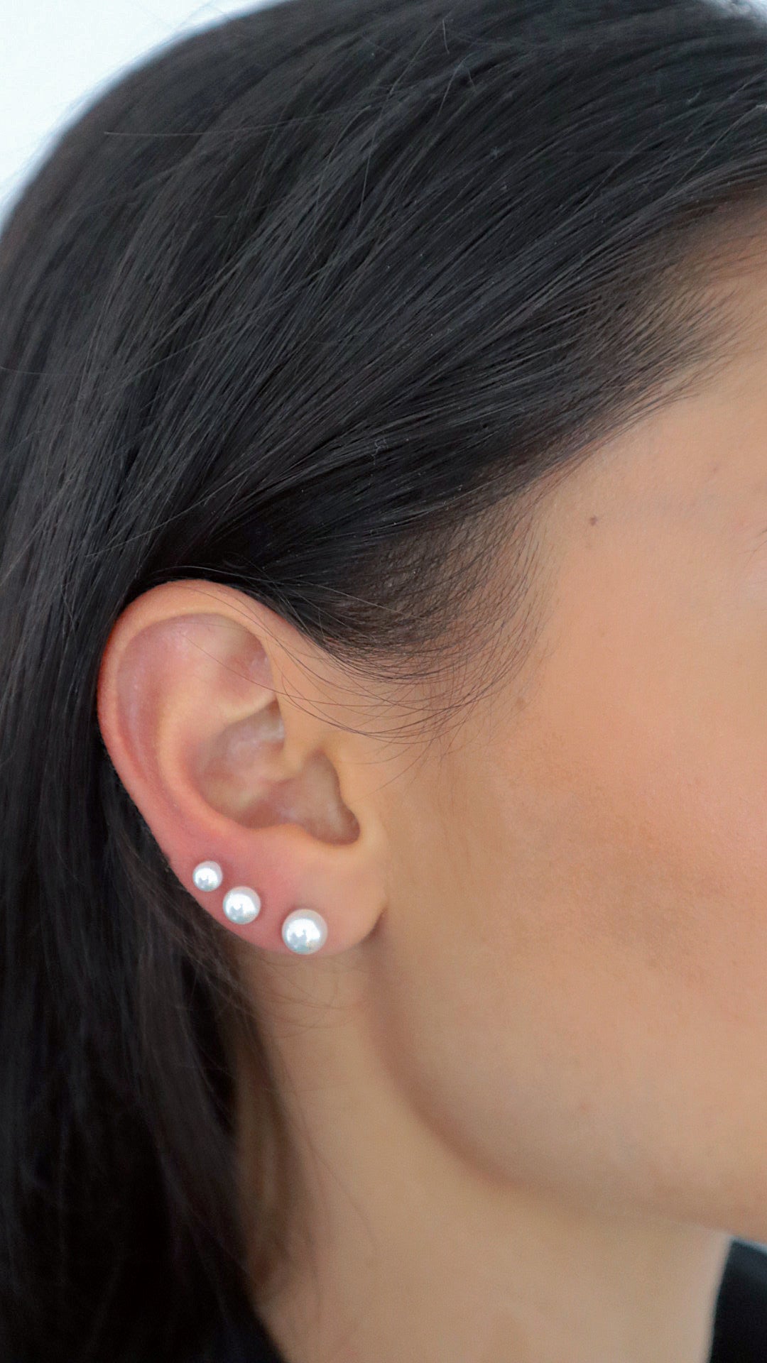 Frau trägt Pearl Balls Perlen Ohrstecker in Silber und Gold im Ohrläppchen, moderner Ear-Stacking-Look.