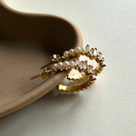 Goldene Pearl X Baguette Ohrringe mit Perlen und Zirkonia, liegend auf Keramik-Schale.