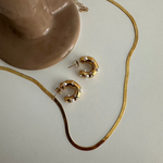 Goldene Perl Zirkonia Creolen mit passender Kette als Flatlay auf hellem Untergrund.