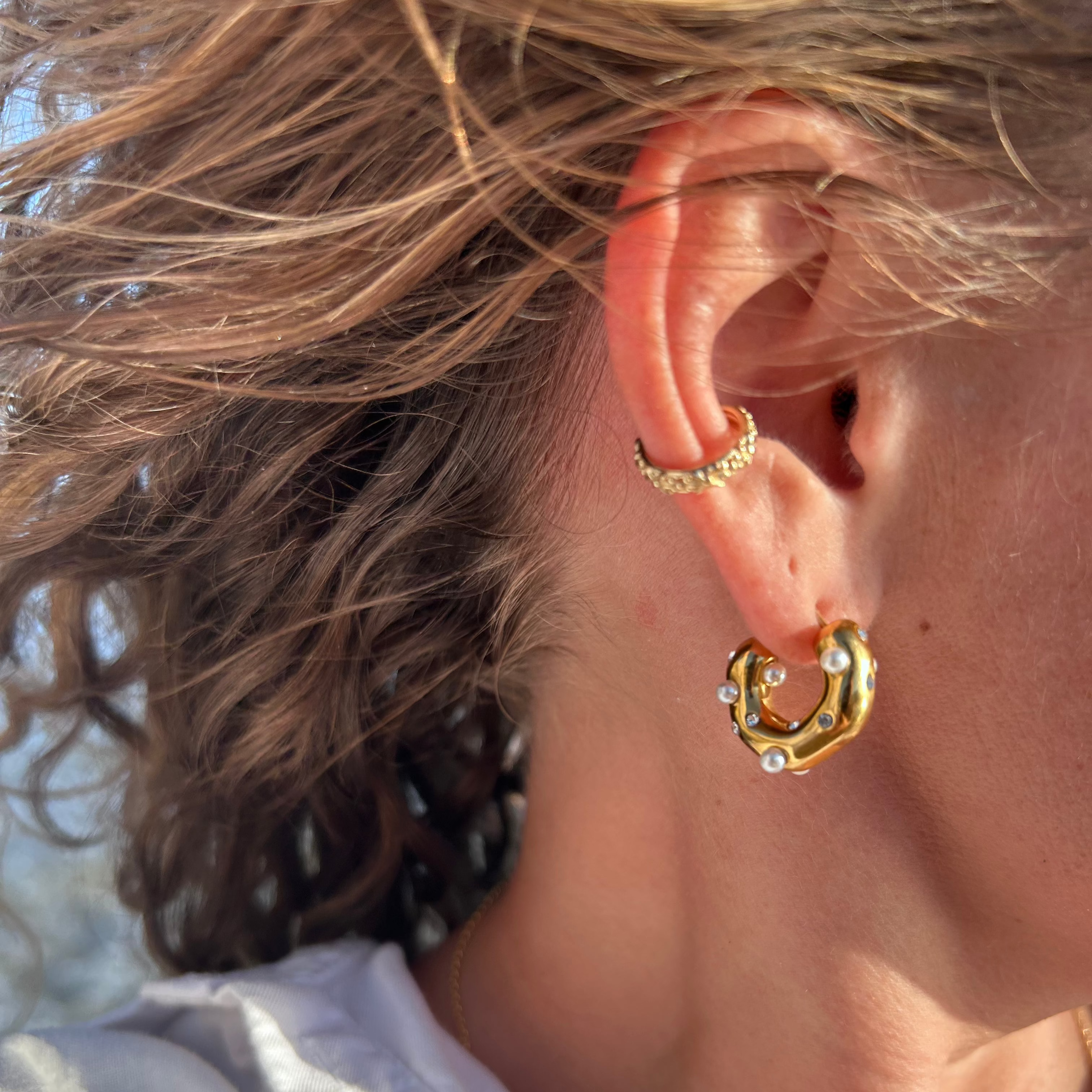 Nahaufnahme eines Ohrs mit Perl Zirkonia Creolen Gold im Sonnenlicht, Haare im Wind.