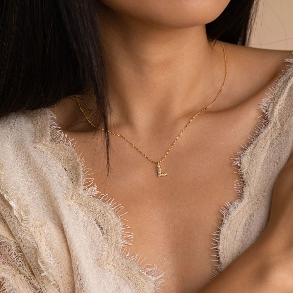 Goldene Perlen Buchstabenkette mit L-Anhänger, getragen an zartem Dekolleté.