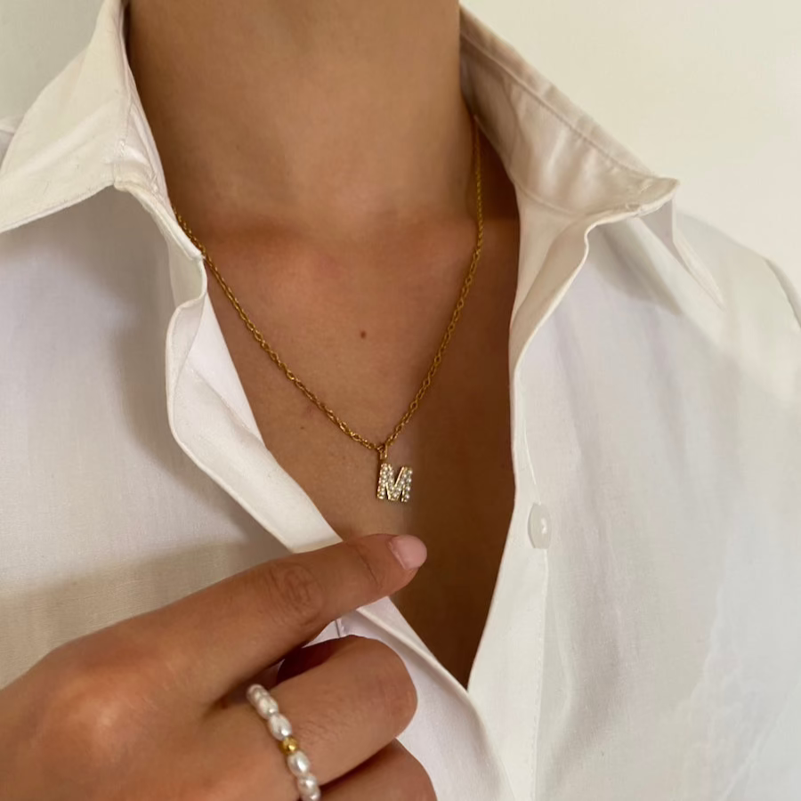 Goldene Perlen Buchstabenkette mit M-Anhänger, getragen zu weißer Bluse.