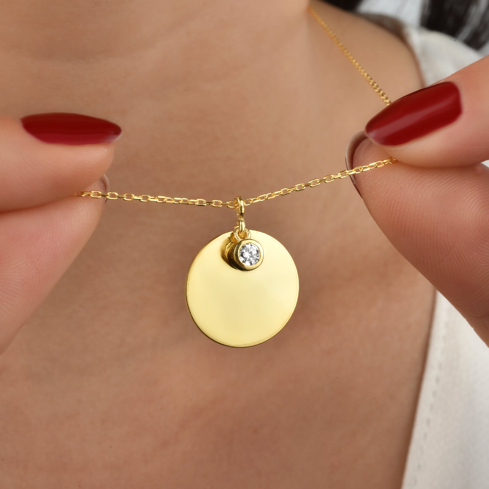 Detailaufnahme: runde Goldkette mit Zirkonia Stein Anhänger zwischen den Fingern – funkelnd.