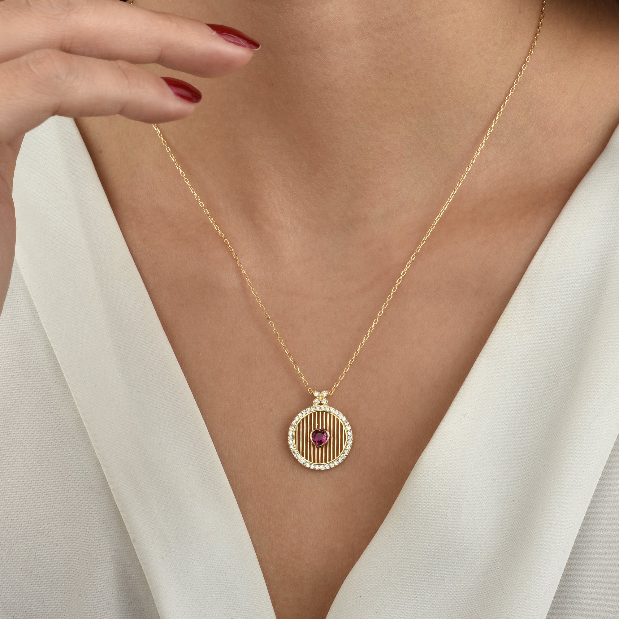 Am Hals getragen: Goldene runde Herz-Kette mit rotem Zirkonia, elegant getragen am Dekolleté.