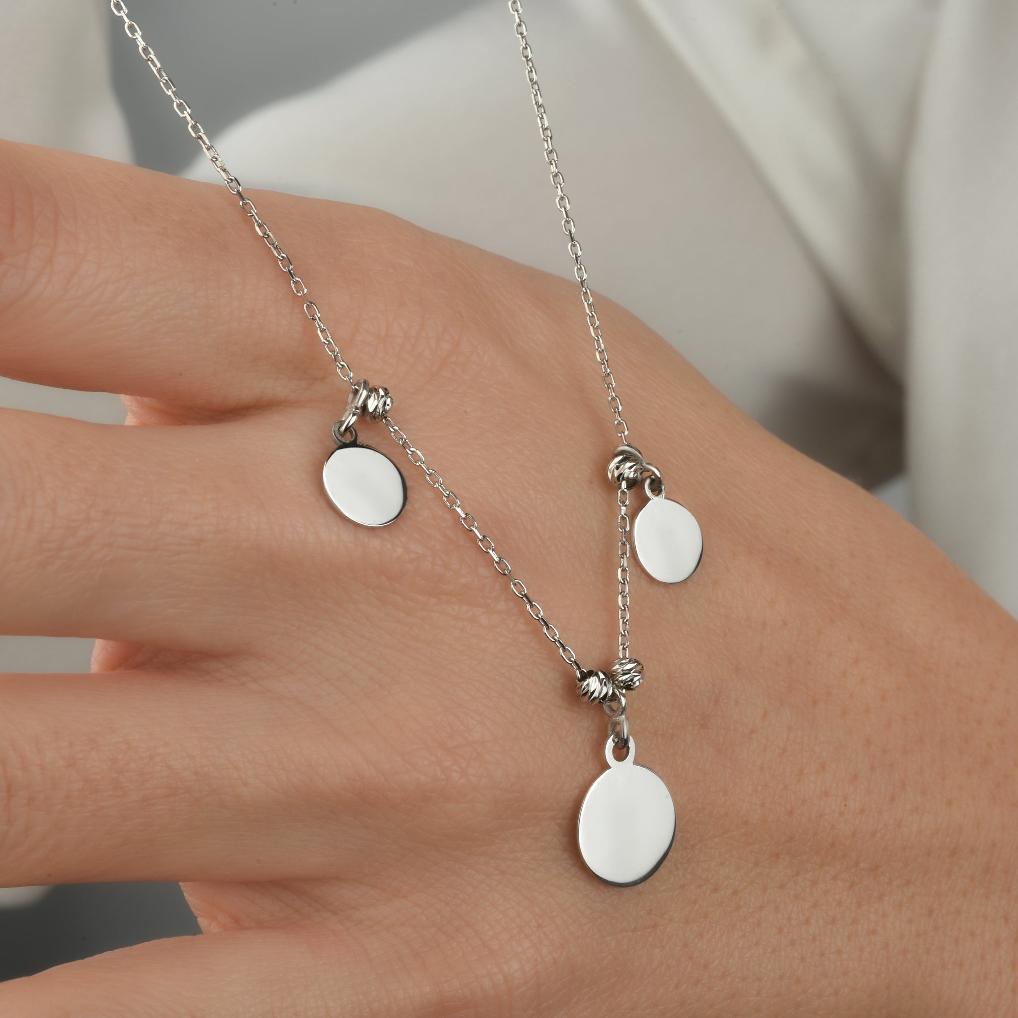 Silberne Plättchen Kette mit drei Anhängern als Detailaufnahme auf der Hand.