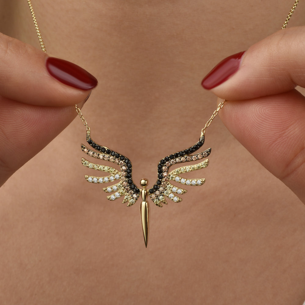 Close-up: Schutzengel Anhänger in Gold mit farbigem Zirkonia-Mix, gehalten zwischen zwei Fingern.