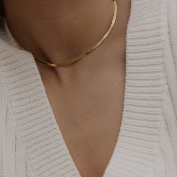 Sleek Halskette Gold am Hals, Close-up mit cremefarbenem Strickpullover.