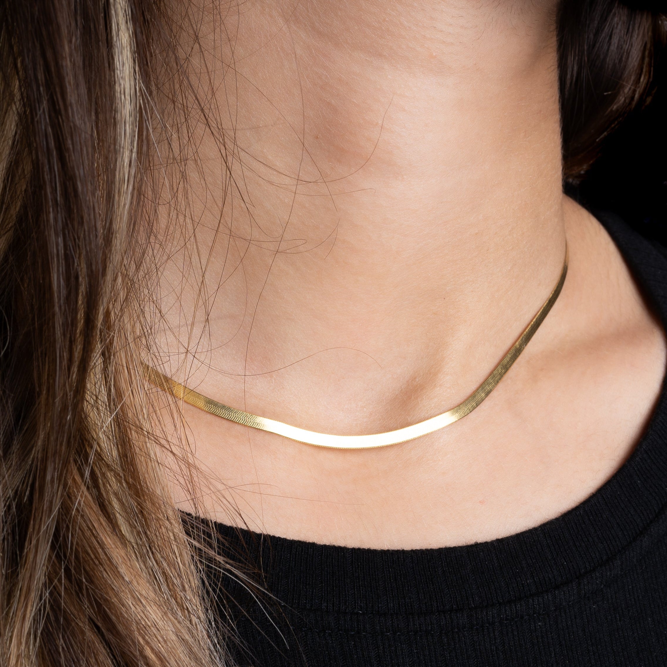 Sleek Halskette Gold als flache Kette am Hals, Close-up mit schwarzem Oberteil.