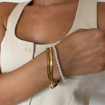 Goldenes Snake Armband aus Edelstahl im Layering mit Perlenarmband am Damenhandgelenk.