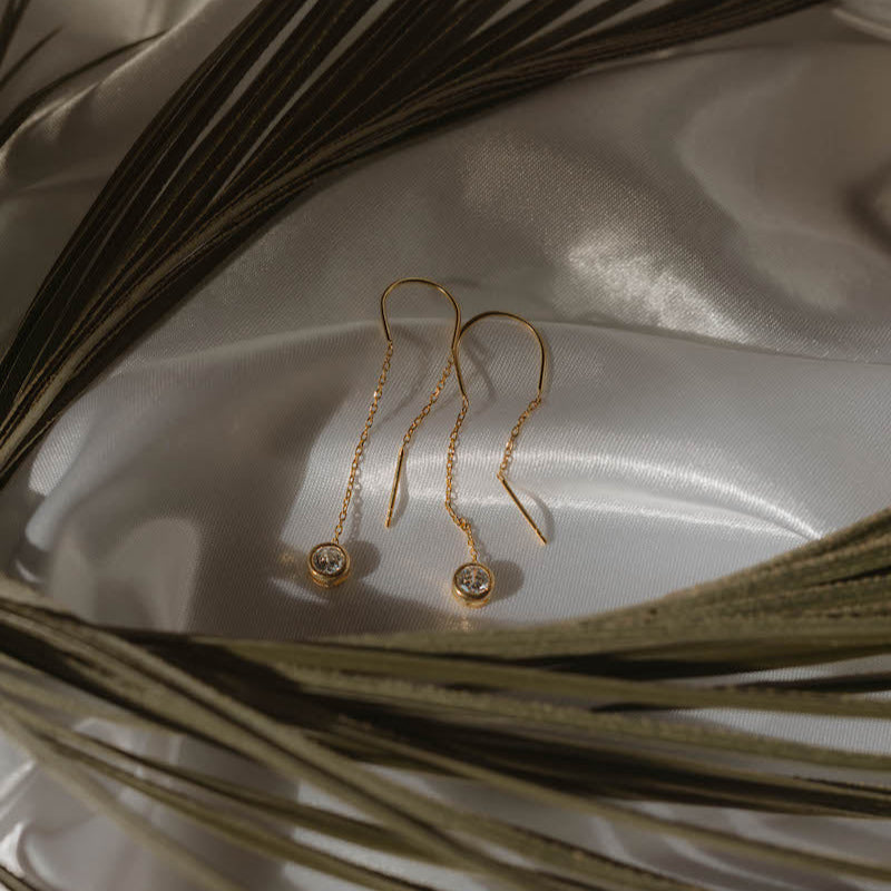 Paar Solitär Ohrringe Gold auf Satin drapiert, Zirkonia Anhänger im Fokus.