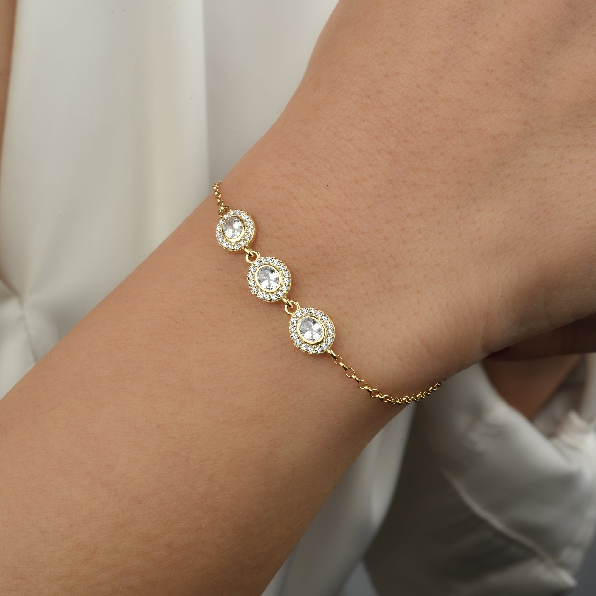 Nahaufnahme: Solitaire Kranz Oval Armband Gold am Handgelenk, drei ovale Zirkonia-Elemente in Reihe.