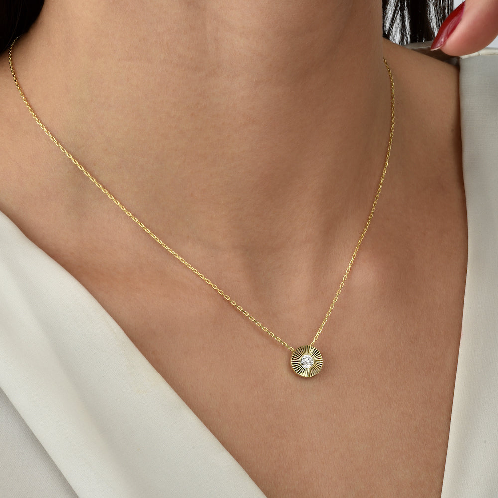 Goldene Solitaire Sun Halskette mit kleinem Sonnen-Anhänger und Zirkonia am Hals einer Frau.