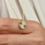 Goldene Solitaire Sun Halskette mit Sonnenstrahlen-Anhänger und Zirkonia auf einem Finger vor hellem Stoff.