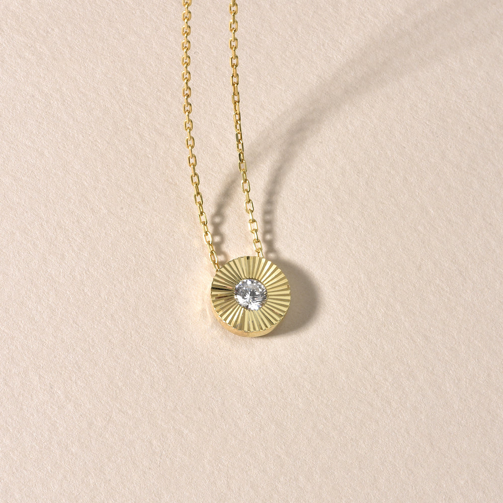 Solitaire Sun Halskette Gold mit rundem Zirkonia-Anhänger dekorativ auf beigem Hintergrund platziert.