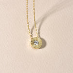 Solitaire Sun Halskette Gold mit rundem Zirkonia-Anhänger dekorativ auf beigem Hintergrund platziert.