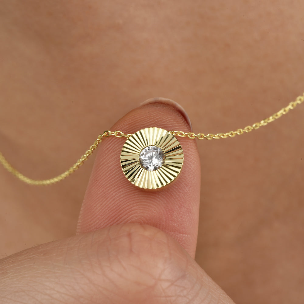 Feine goldene Halskette mit rundem Sonnenstrahlen-Anhänger und funkelndem Zirkonia zwischen Fingern gehalten.
