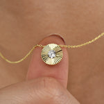 Feine goldene Halskette mit rundem Sonnenstrahlen-Anhänger und funkelndem Zirkonia zwischen Fingern gehalten.