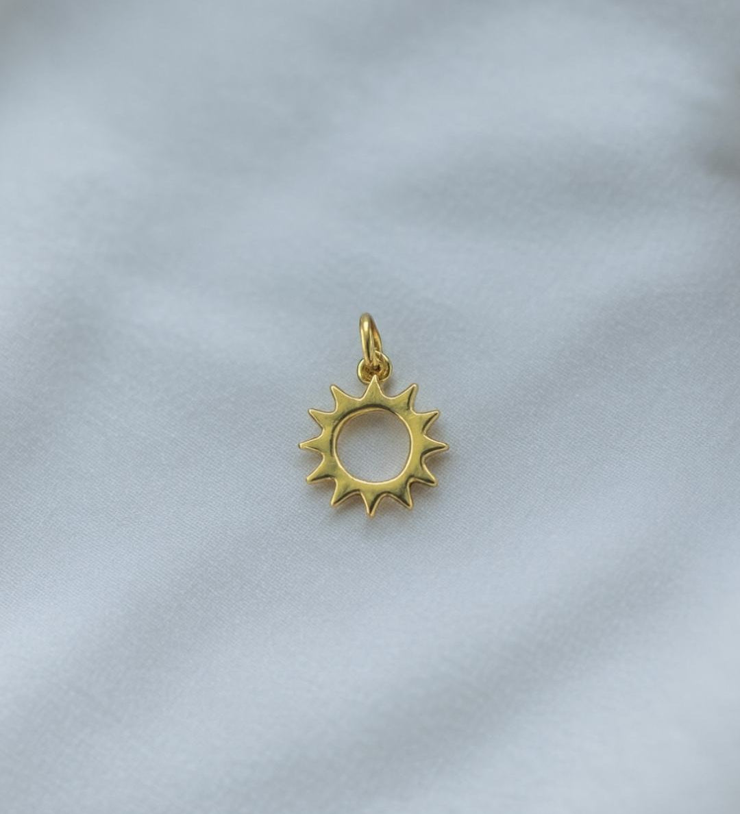 Goldener Sonnen Charm aus der Rio de Janeiro Kollektion, fotografiert auf hellem Stoff, hochwertige Vergoldung im Detail.
