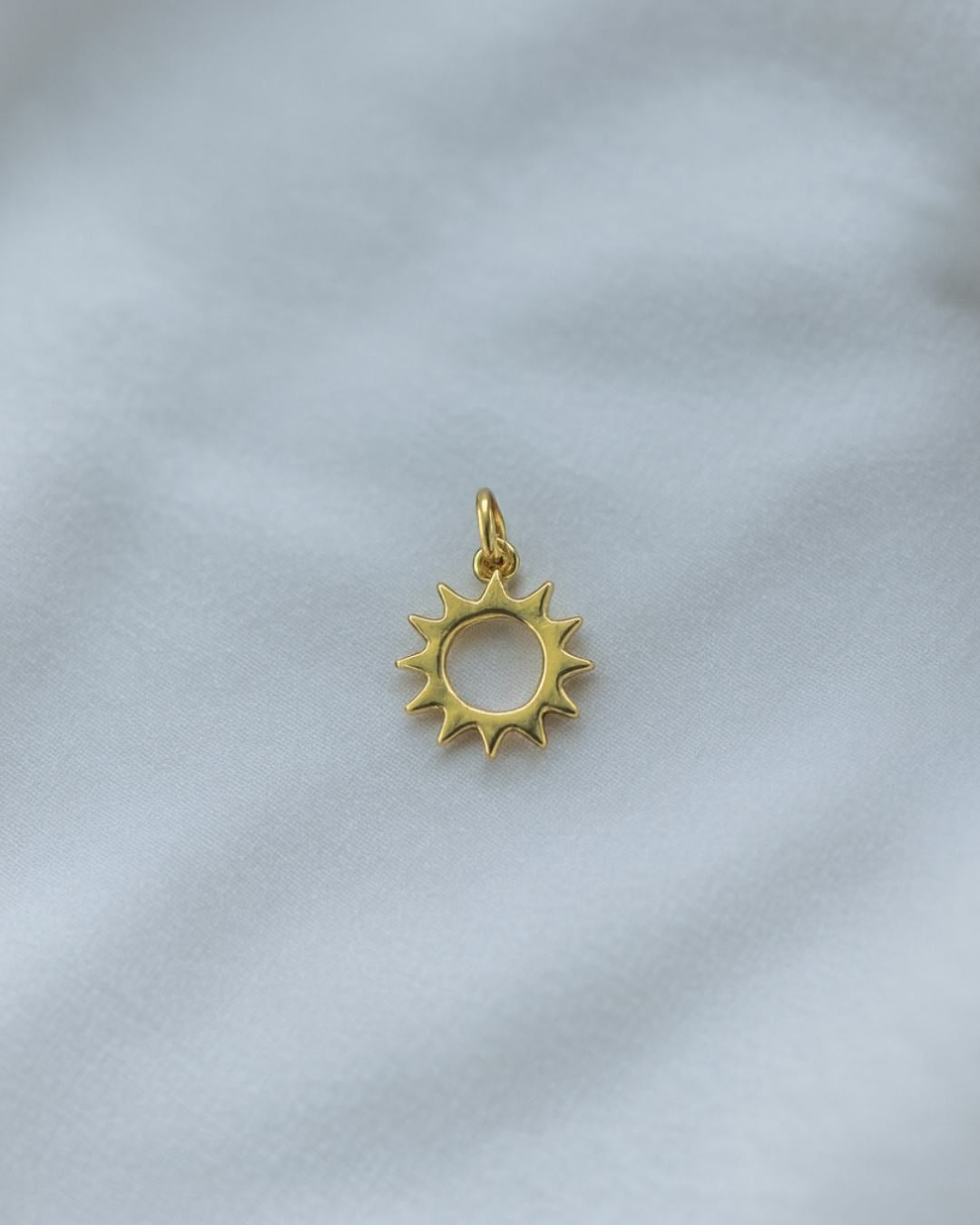 Goldener Sonnen Charm aus der Rio de Janeiro Kollektion, fotografiert auf hellem Stoff, hochwertige Vergoldung im Detail.