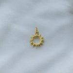 Goldener Sonnen Charm aus der Rio de Janeiro Kollektion, fotografiert auf hellem Stoff, hochwertige Vergoldung im Detail.