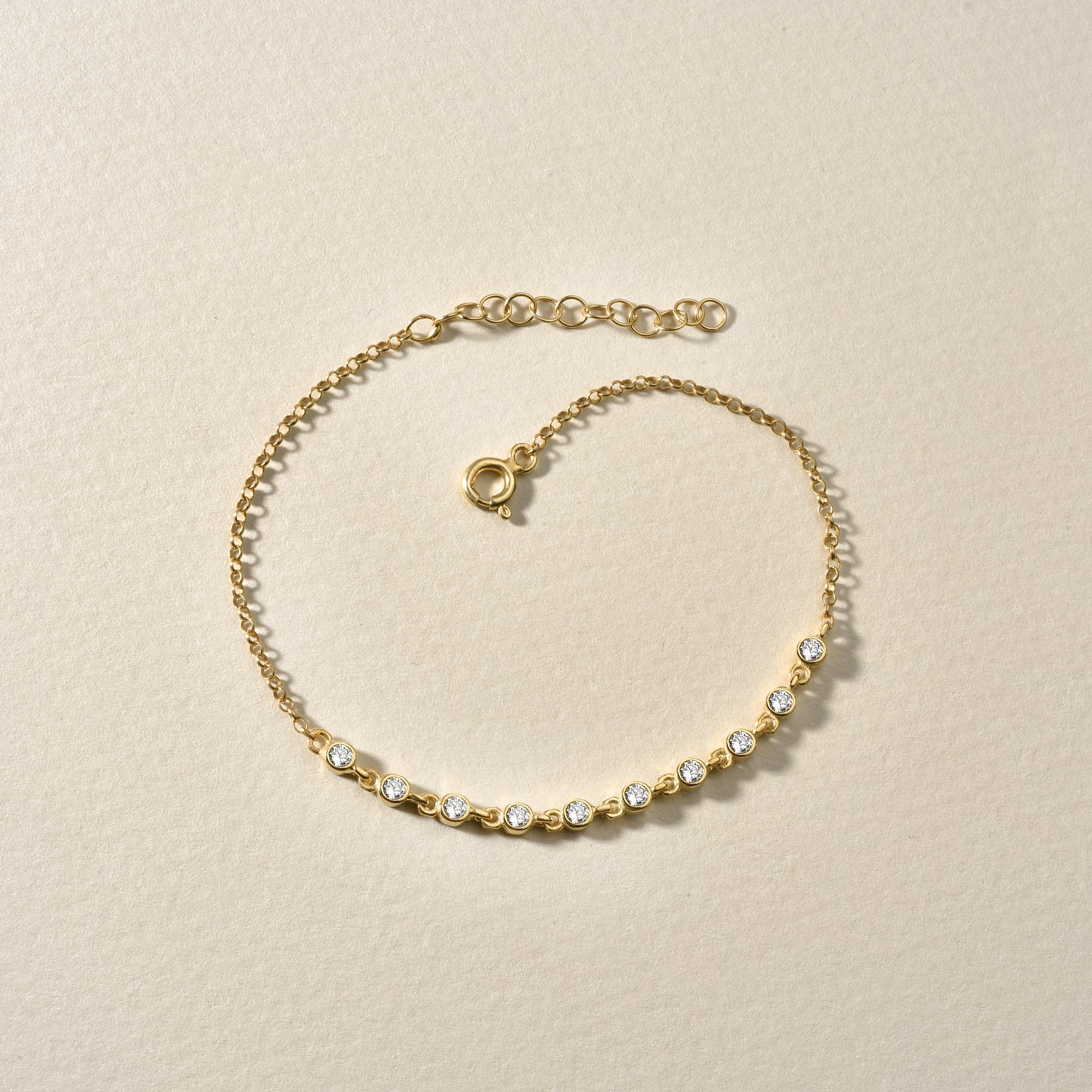 Filigranes Sparkle Zirkonia Armband Gold flach liegend auf beigem Untergrund.