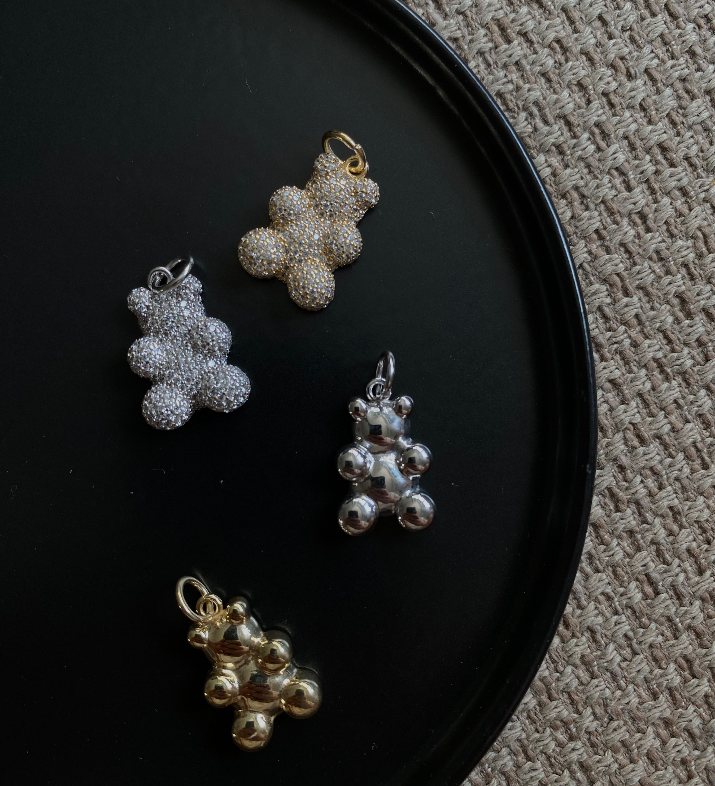 Vier Sparkling Bear Anhänger in Silber, Gold und glänzendem Metall auf schwarzem Teller.