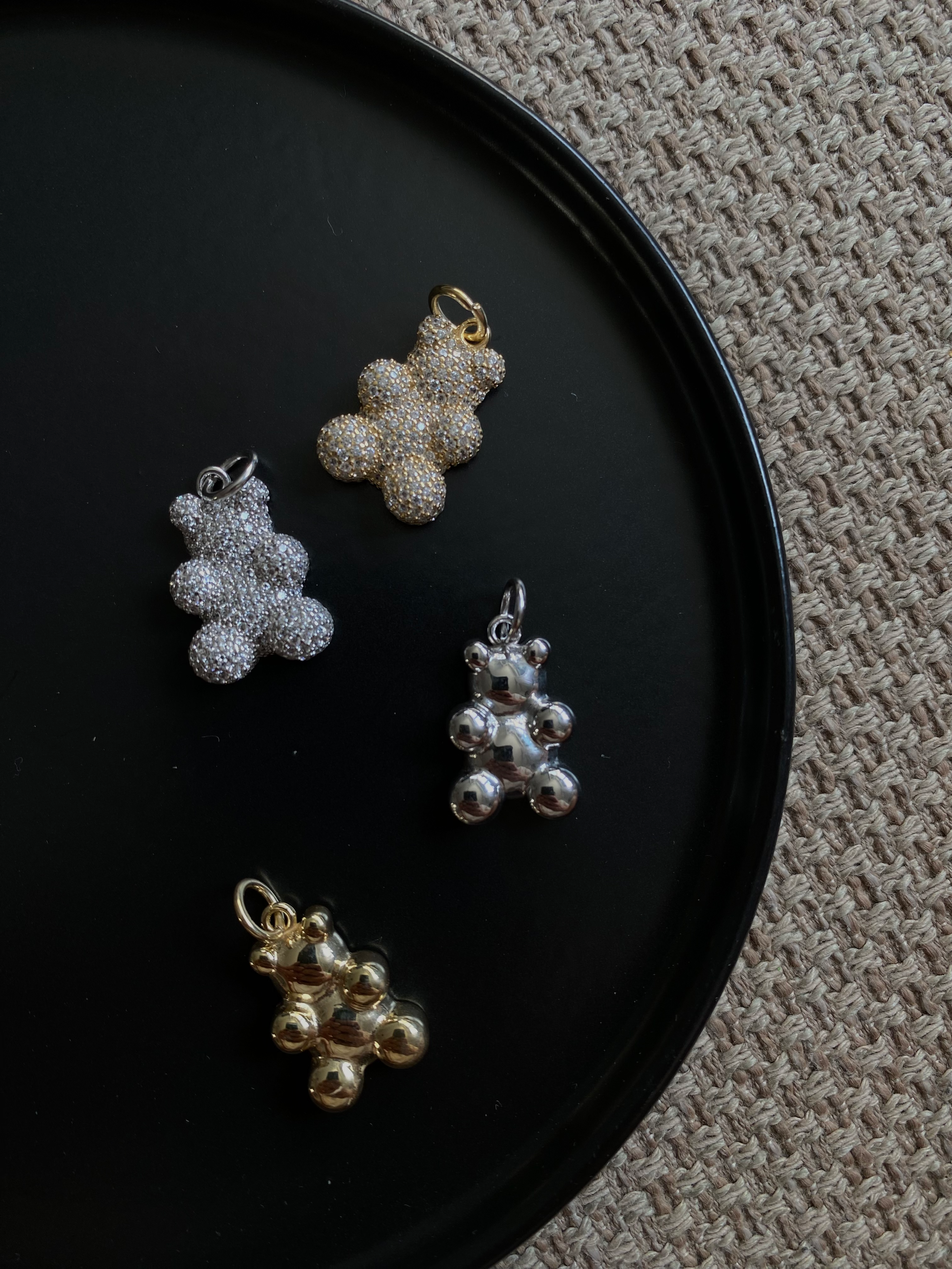 Vier Sparkling Bear Anhänger in Silber, Gold und glänzendem Metall auf schwarzem Teller.
