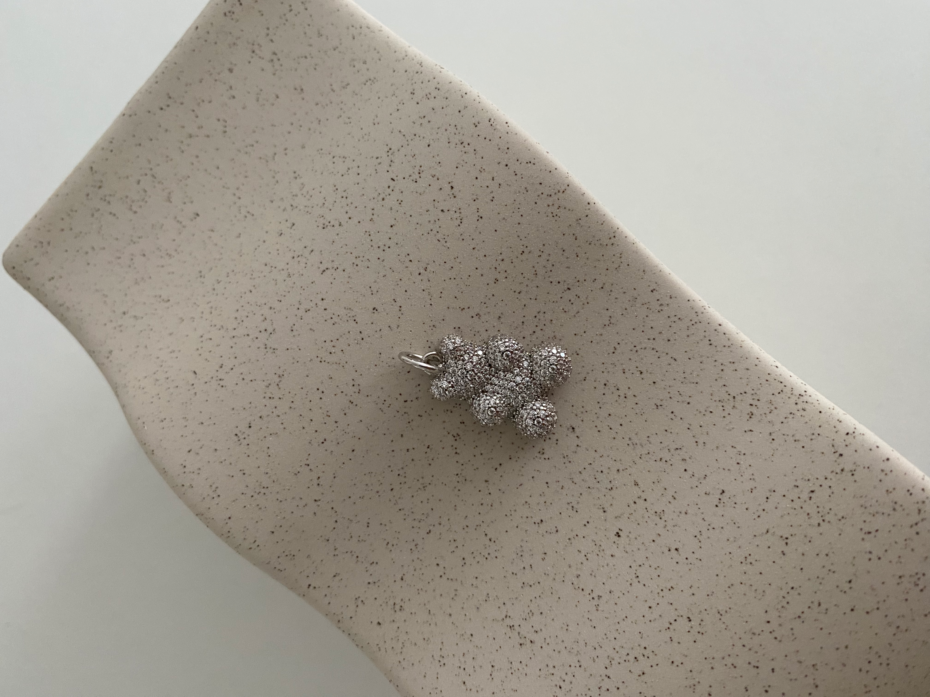 Silberner Sparkling Bear Anhänger mit Zirkonia auf beiger, strukturierter Keramikablage.