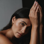 Frau stützt den Kopf auf die Hände und trägt goldene Square Hoop Ohrringe, warmer Lichtlook.