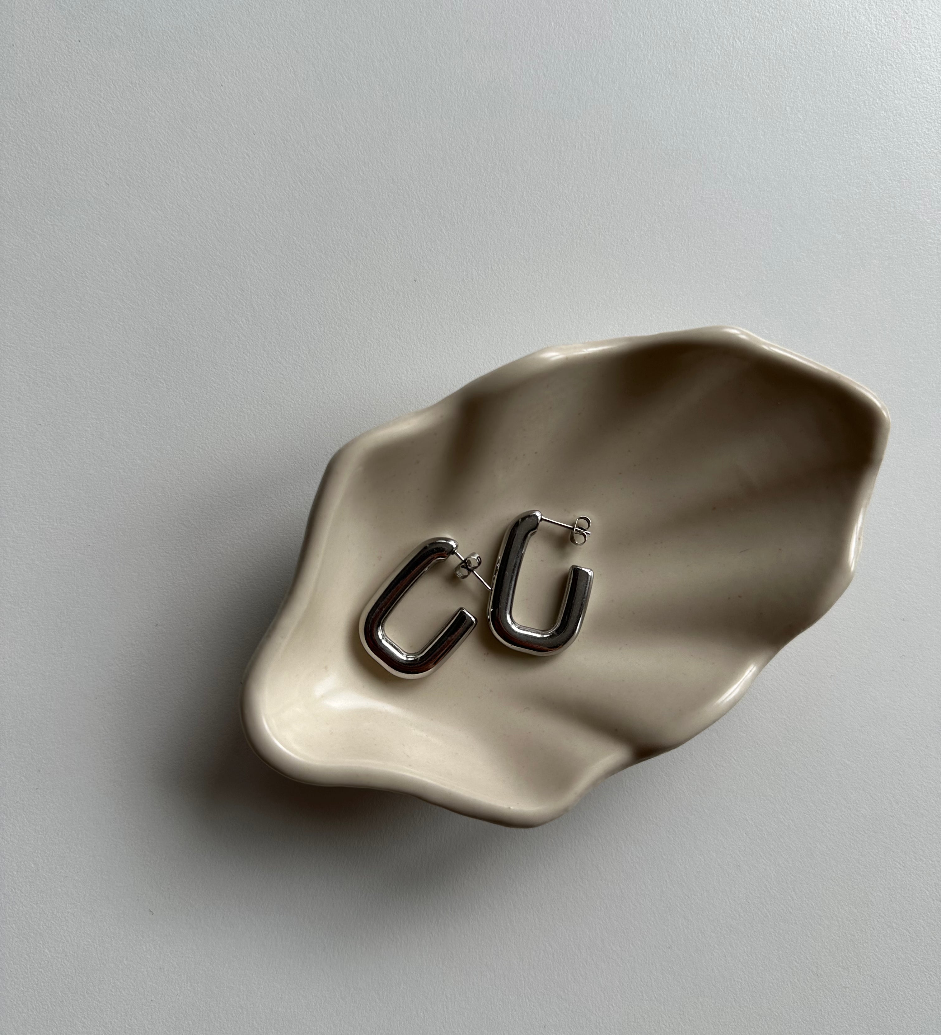 Silberne Square Hoop Ohrringe auf beiger Schmuckschale, minimalistisches Flatlay.