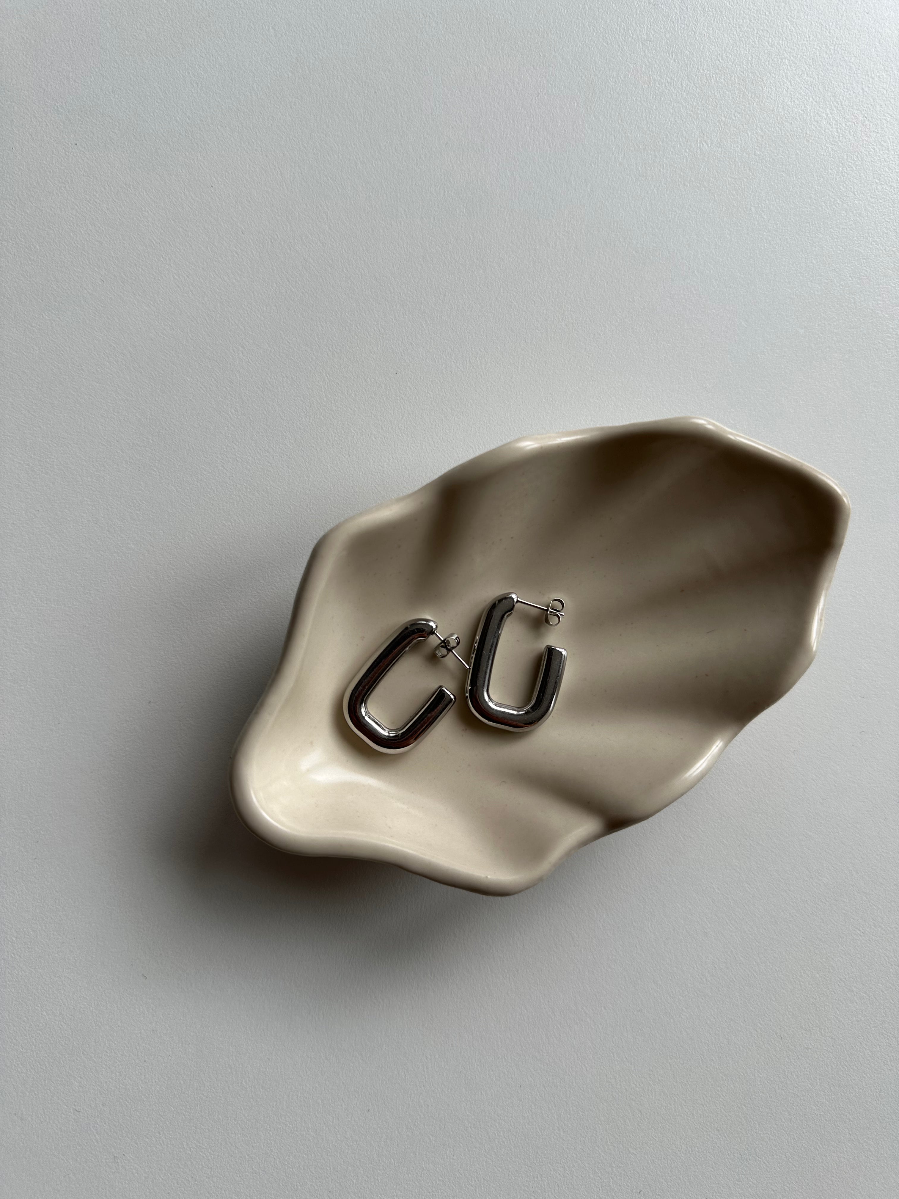 Silberne Square Hoop Ohrringe auf beiger Schmuckschale, minimalistisches Flatlay.