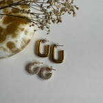 Goldene Square Hoop Ohrringe und Perlencreolen neben dekorativer Vase auf hellem Untergrund.