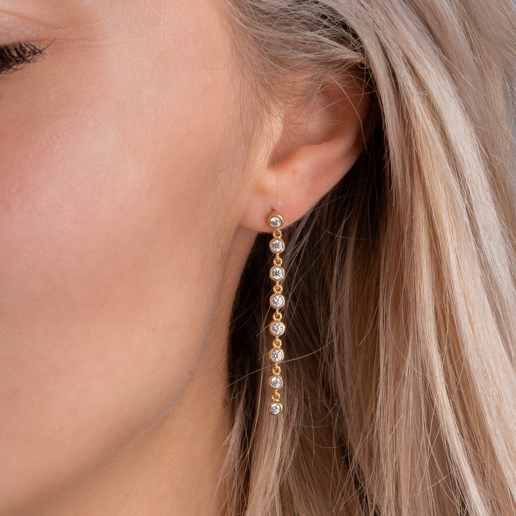 Model trägt Tennis Ohrringe Zirkonia rund klein Gold – elegante, lange Ohrhänger am Ohr.