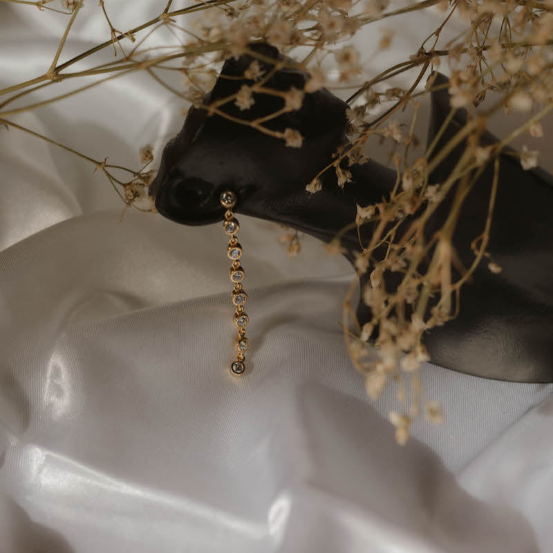 Tennis Ohrringe Zirkonia rund klein Gold – Stylingfoto vor zartem Blumen-Set.