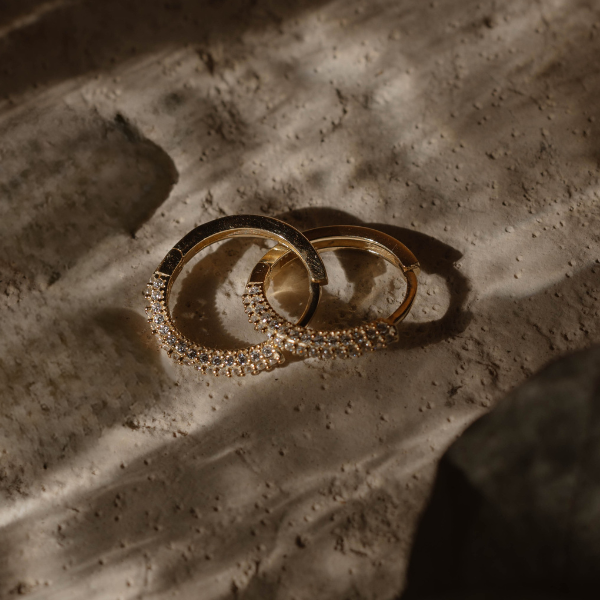 Goldene Pavé Creolen mit Zirkonia auf Stein – eleganter Schmuck Look, warmes Licht und Schatten.