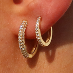 Nahaufnahme: kleine goldene Pavé Creolen mit Zirkonia – funkelnder Look am Ohr, alltagstauglich.