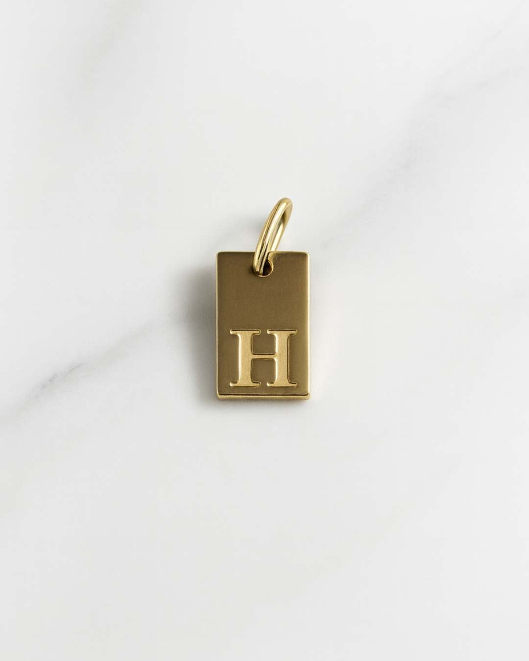 Vergoldeter rechteckiger Initial Charm der Tokio Kollektion auf hellem Marmorfond