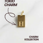 Detailaufnahme des goldenen Tokio Initial Anhängers mit Buchstabenprägung