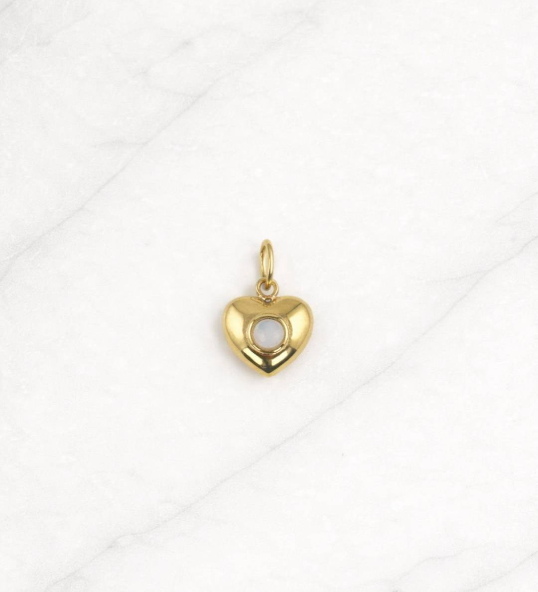 Tulum Charm in Gold mit Herzform und weißem Stein auf hellem Hintergrund.