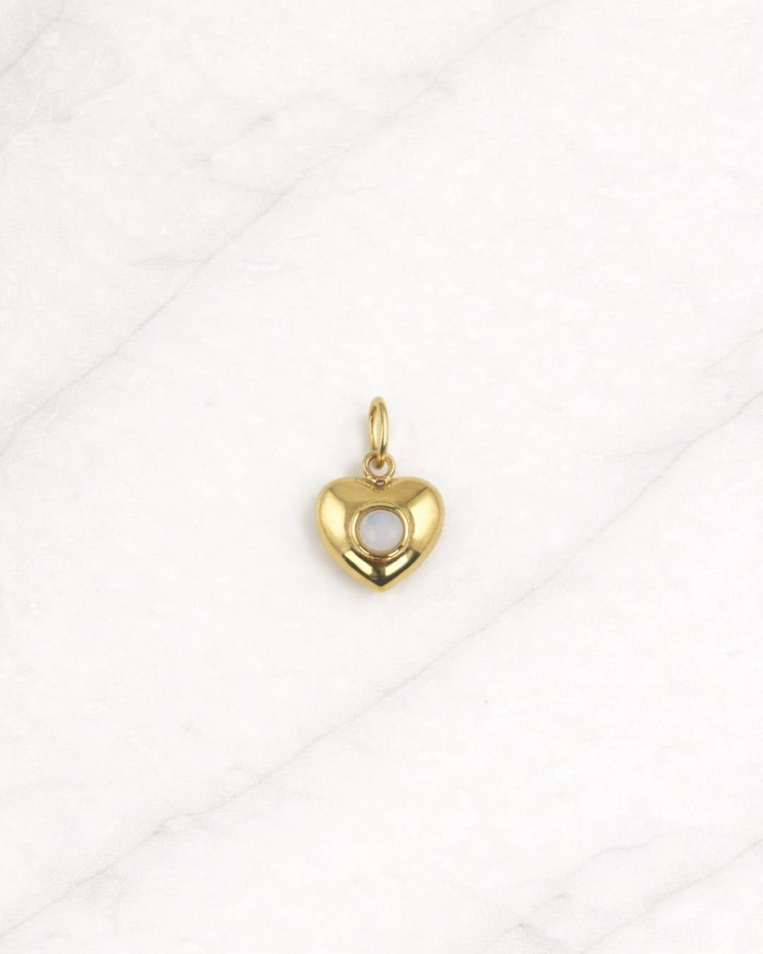 Tulum Charm in Gold mit Herzform und weißem Stein auf hellem Hintergrund.