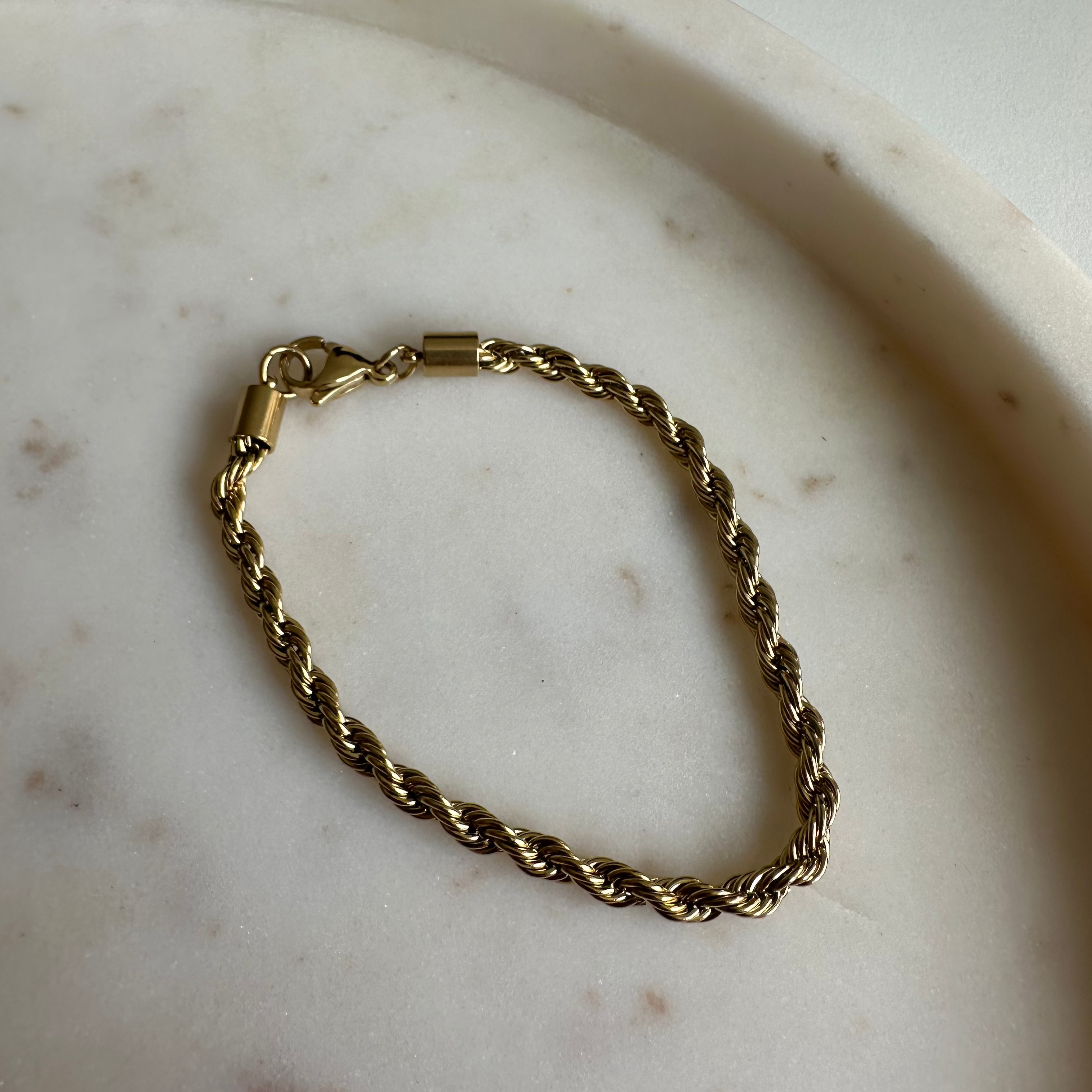 Goldenes Twist Armband auf runder Marmorplatte, gedrehte Glieder gut sichtbar.