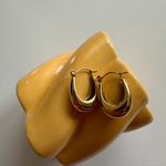 Goldene U Hoop Creolen auf beiger Skulptur, glänzender Vintage-Look für Damen.