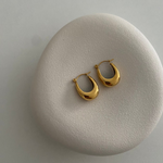 Goldene U Hoop Ohrringe auf hellem Stein-Display, minimalistische Produktaufnahme für Damen.