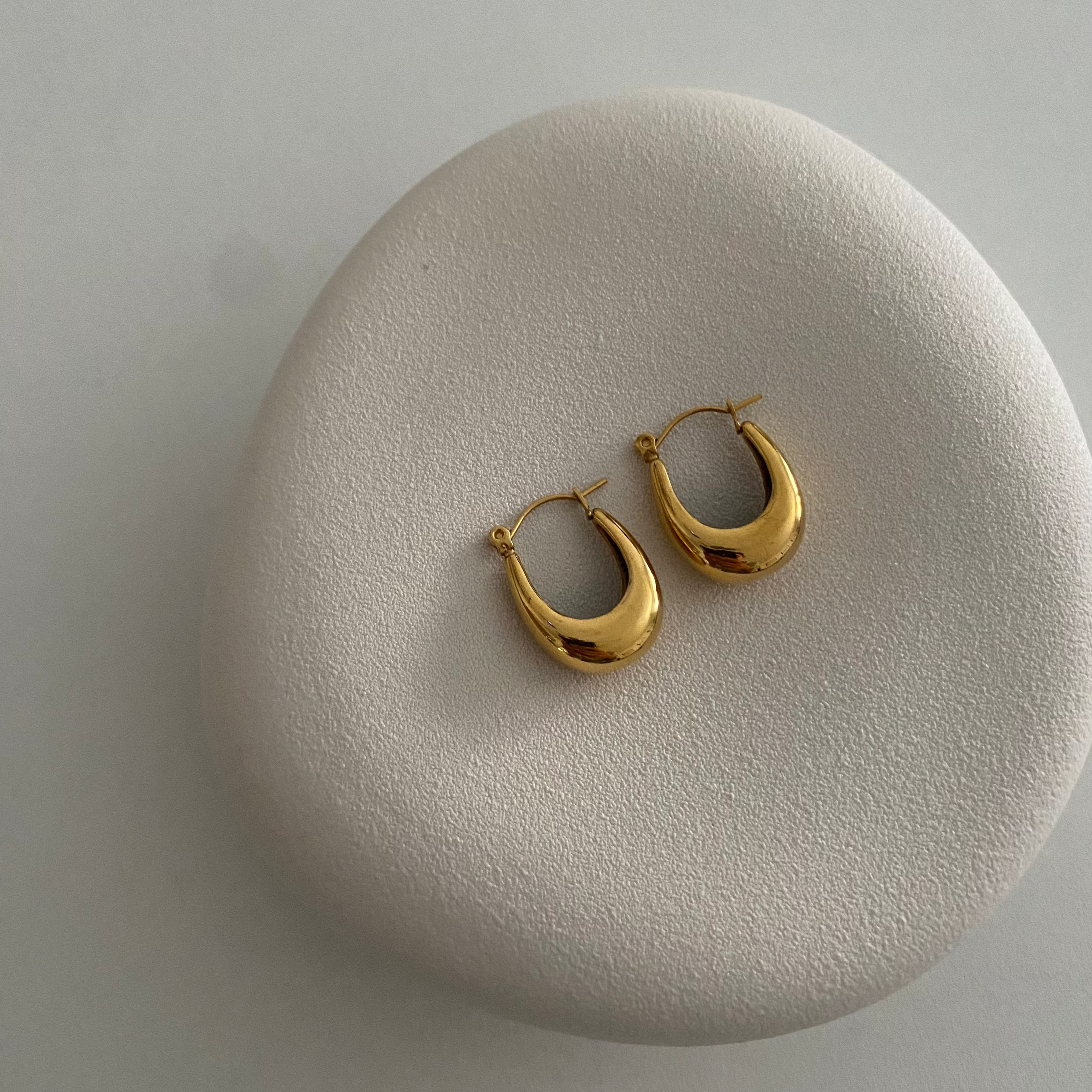 Goldene U Hoop Ohrringe auf hellem Stein-Display, minimalistische Produktaufnahme für Damen.