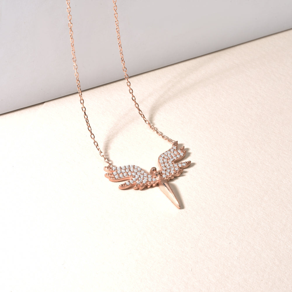 White Angle Kette – Rosé mit funkelndem Engelsflügel-Anhänger liegend auf hellem Stoff