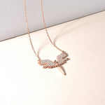 White Angle Kette – Rosé mit funkelndem Engelsflügel-Anhänger liegend auf hellem Stoff