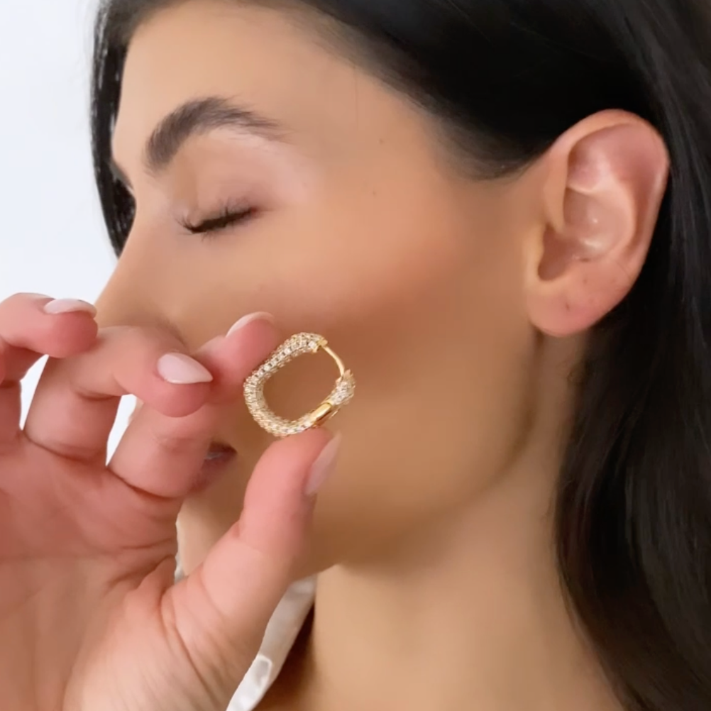 Frau hält einen goldenen eckigen Zirkonia Hoop Ohrring nah am Gesicht als Tragebild.