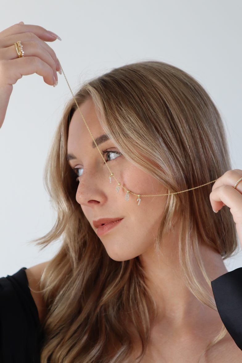 Modell mit goldener Halskette und mehreren Charm Numbers Ziffern im Gesicht.