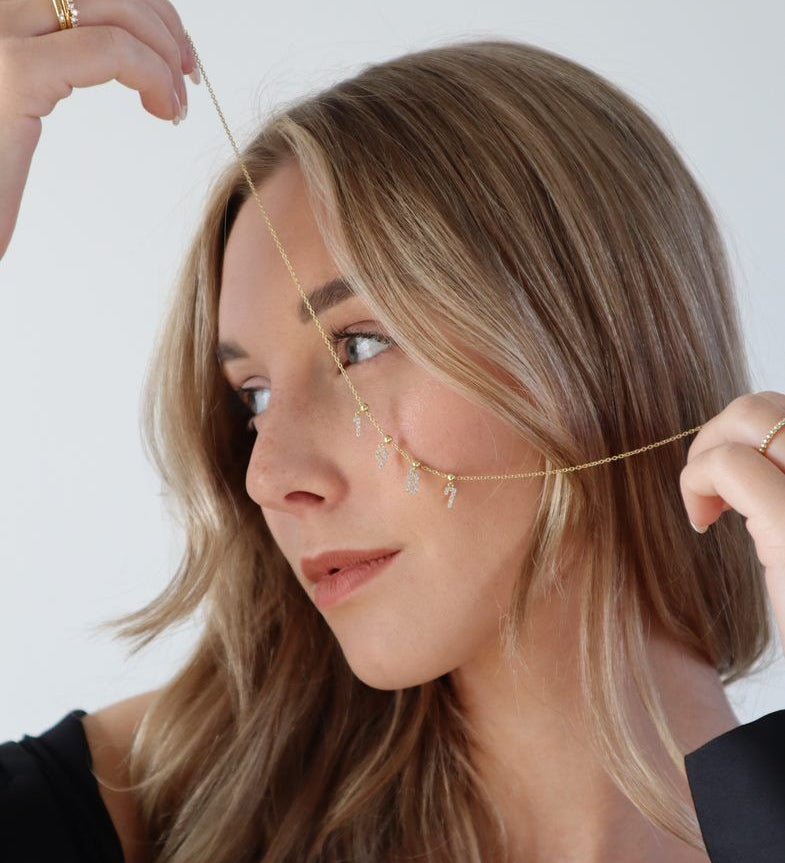 Modell mit goldener Halskette und mehreren Charm Numbers Ziffern im Gesicht.